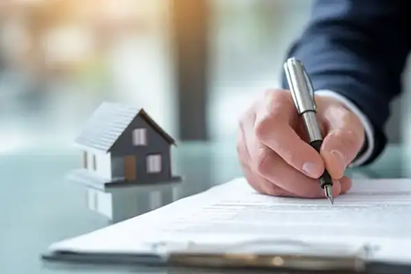 Person unterschreibt Dokument neben Modellhaus